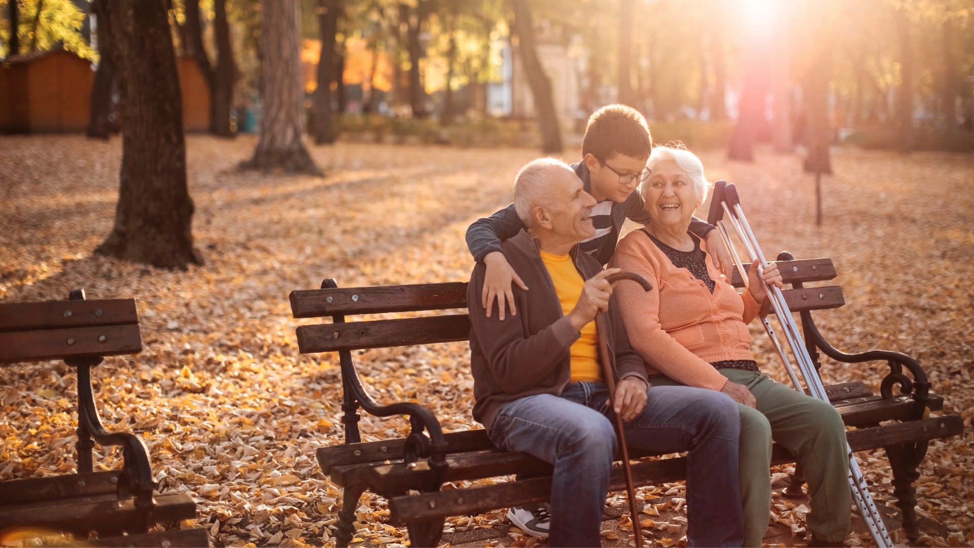 Two elderly people sitting on a park bench with a young boy during Autumn.